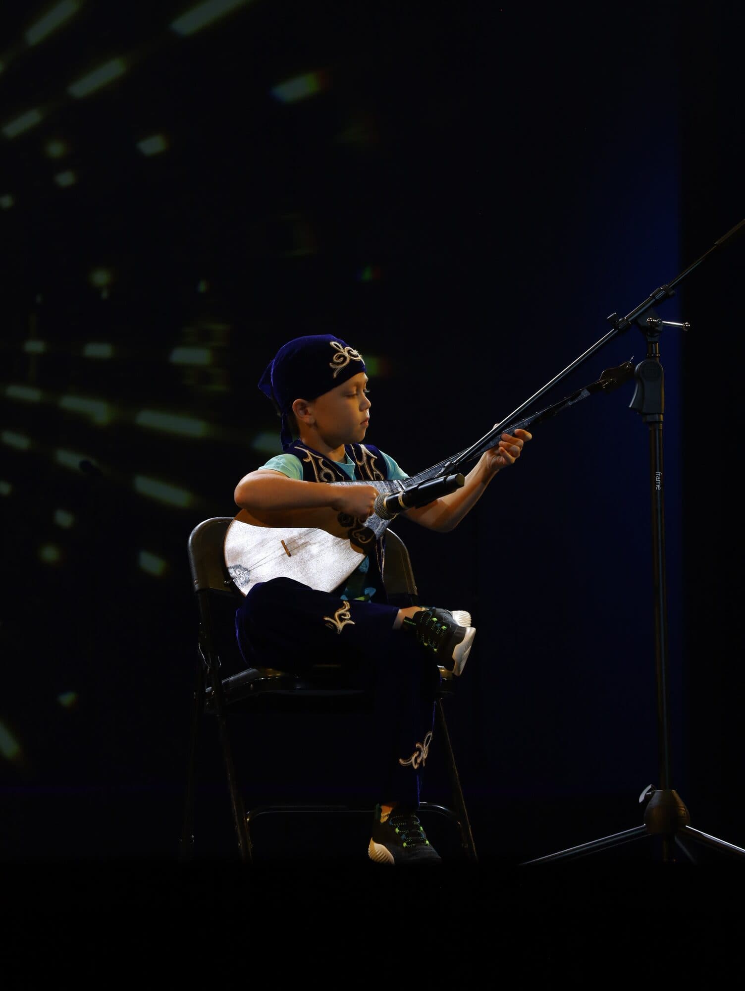 A boy in traditional dress plays a long-necked lute on stage
