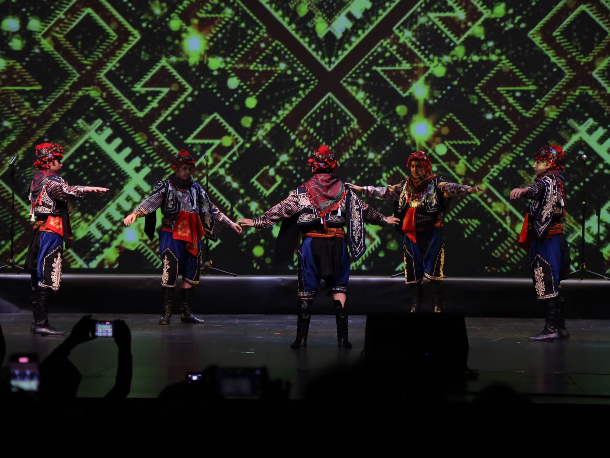 A folk dance troupe in traditional costume links arms on stage