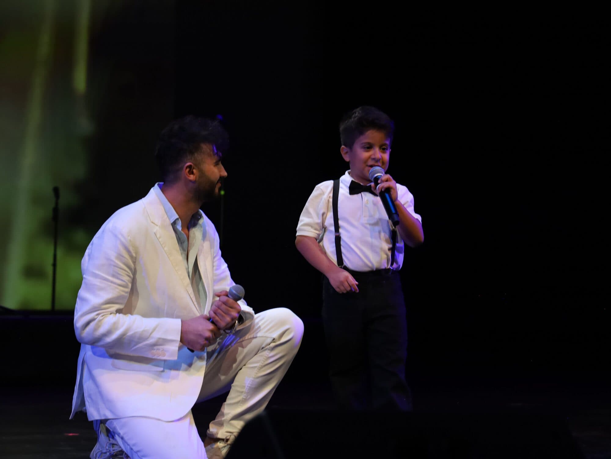 A mentor kneels beside a young boy as they sing a duet